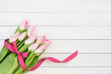 Bouquet of pink tulips decorated with ribbon on white wooden background. Top view, copy space
