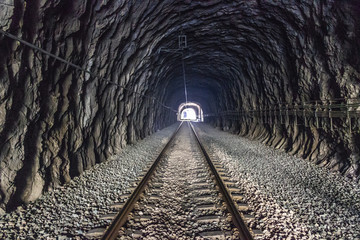 Interior of a railway tunnel inside a natural mountain with the track ending in the infinity light....