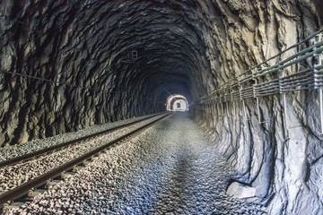 Interior of a railway tunnel inside a natural mountain with the track ending in the infinity light....