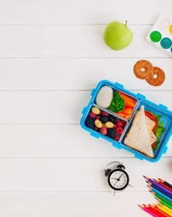 Gordijnen Lunch box with sandwich, vegetables, berries on white wooden background with clock, watercolor and pencils © lithiumphoto