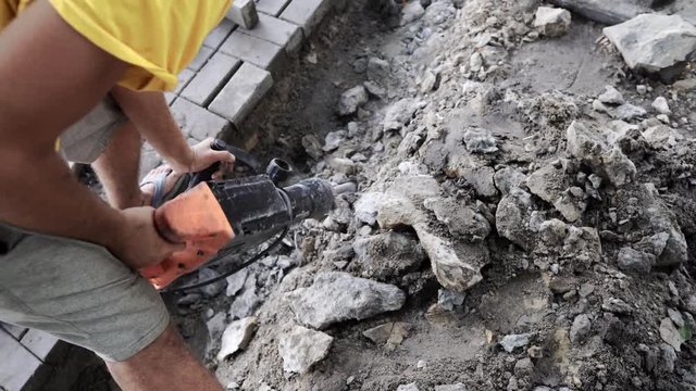 Workers use Electric Concrete Breaker. Male worker repairing driveway surface with jackhammer, digging and drilling concrete roads during sidewalk construction works.