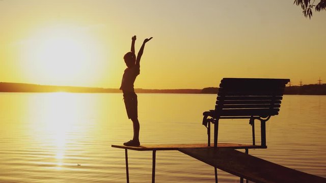 boy are doing physical activities on the bridge near the bench on the background of sunset by the river