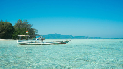 Fototapeta na wymiar traditional boat transportation on the shallow sea with transparent clear and island in distance