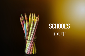 Concept of School holiday  with inscription, color pencils on black background with flare. .