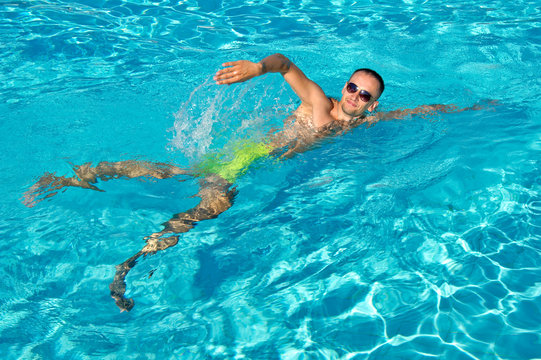 Young man in sunglasses swimming in outdoor pool