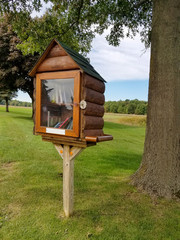 log cabin birdhouse library on wooden post in rural field