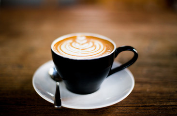 Cup of hot cappucino is standing on the wooden table.
