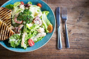 Fresh caesar salad in the plate on dark wooden table.