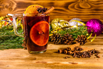 Cup of mulled wine with cinnamon, christmas decorations and fir tree branches on wooden table