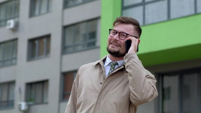 Young cheerful businessman talking on his phone outdoors. 4k UHD.