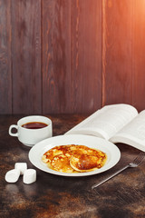 Pancakes with honey on white plate, tea and book