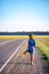 Obraz premium Beautiful elegant woman walking on a country road. redhaired girl in the field wreath of sunflowers and bouquet of sunflowers, dressed in a dress-shirt made of denim and red rubber boots