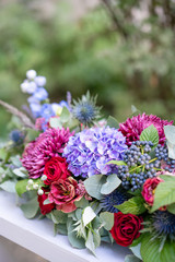 Elongated floral arrangement in vintage metal vase. table setting. Blue and red color. Gorgeous bouquet of different flowers. Park on background