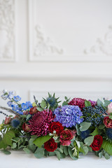 Elongated floral arrangement in vintage metal vase. table setting. Blue and red color. Gorgeous bouquet of different flowers. Bright room, stucco on the wall