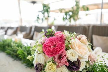 Arrangement of fresh flowers in pastel colors with a bright accent. Wedding background. table in a restaurant. different varieties of garden and shrub roses in a light vase on wooden table