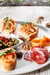Plate with Italian appetizers. Bruschetta with a cherry tomatoes and shrimps. Parmesan cheese, prosciutto, green capers, olives, sun-dried tomatoes and walnuts.