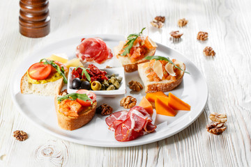 Plate with Italian appetizers. Bruschetta with a cherry tomatoes and shrimps. Parmesan cheese, prosciutto, green capers, olives, sun-dried tomatoes and walnuts.