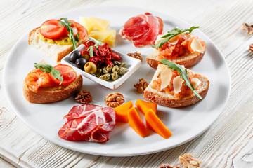 Plate with Italian appetizers. Bruschetta with a cherry tomatoes and shrimps. Parmesan cheese, prosciutto, green capers, olives, sun-dried tomatoes and walnuts.