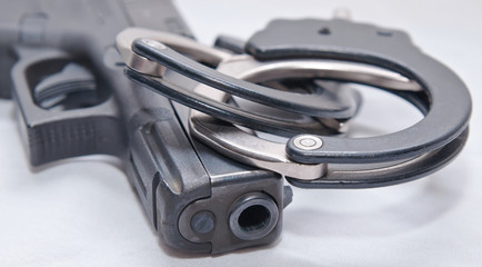 A pair of black and silver handcuffs on top of a black pistol muzzle on a white background