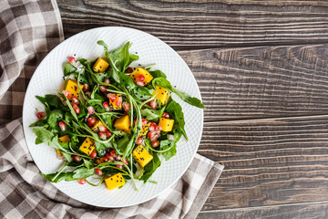 Food flat lay. Top view. Salad with mango, roasted pumpkin, arugula, pomegranate seeds lying on white plate