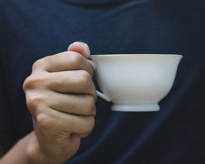 Man holding coffee mug in hand on dark shirt background. Vintage mugs for your design.