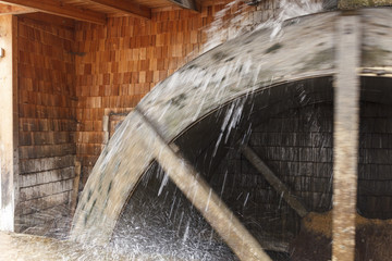 ancient, vintage wood working watermill wheel at which water flows continuously rotating it