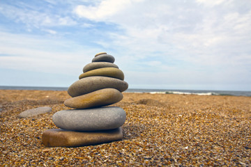 Fototapeta na wymiar Stones pyramid on sand symbolizing zen, harmony, balance. Sea in the background
