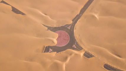 Aerial view of a desert road being run over by sand dunes photographed from a drone at sunrise....