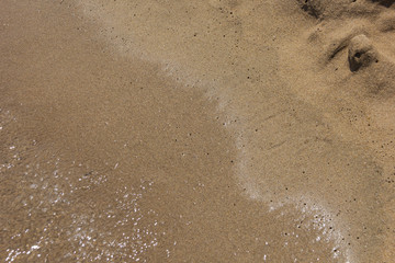 the background image is white the sea foam of the waves lapping on the sandy beach, washing away the footprints in the sand