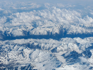 Fototapeta premium view of the snow-covered peaks of the mountains hidden behind the clouds from the window of the plane