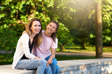 Fototapeta na wymiar A pair of beautiful young girls are laughing and hugging against a green Sunny Park. The concept of friendship, meetings, communication in the open air.
