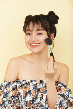 Joyful young Asian woman with cute two buns applying bronzer