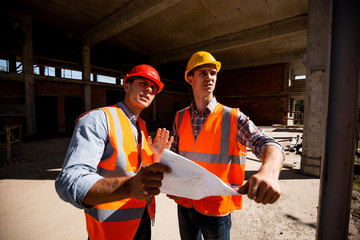Architect  and structural engineer  dressed in orange work vests and helmets work documentation...