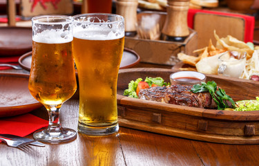 Hot steak with sauce and vegetables. Two glasses of lager beer