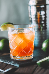 The alcoholic cocktail in a old-fashioned glass among bar tools on a wooden table.