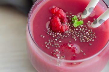Red fruit raspberry smoothie in glass topped with chia seeds and mint on wooden table. Detox drink and health life concept. Close up