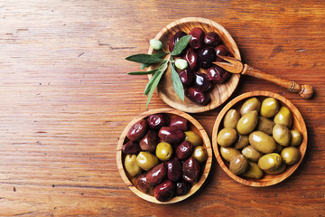Various olives in bowls on wooden kitchen table top view.
