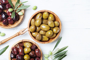 Olives in wooden bowls decorated with olive tree branch top view.