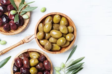 Poster Olives in wooden bowls decorated with olive tree branch top view. © juliasudnitskaya