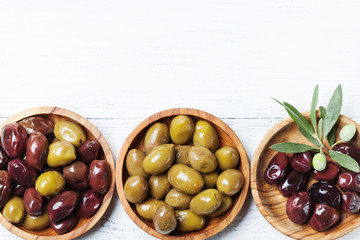 Olives in wooden bowls on white wooden table top view.