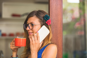 Woman using cellphone and drinking coffee inside the apartment - window, glass, reflection.