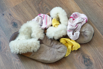 Old fur women's house slippers and socks lie a bunch on the wooden floor