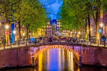 Fototapeta premium Kanał Amsterdamu z typowymi holenderskimi domami i mostem podczas niebieskiej godziny zmierzchu w Holandii, Holandia