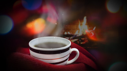 A cup of tea wrapped in a warm winter scarf on a bokeh background. Winter cozy background.