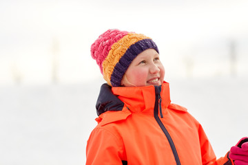 childhood, leisure and season concept - portrait of happy little girl in winter clothes outdoors