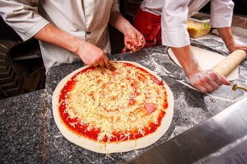 Adding cheese to pizza. Dough on the table.