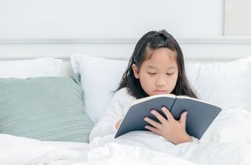 Little asian girl read book on bed