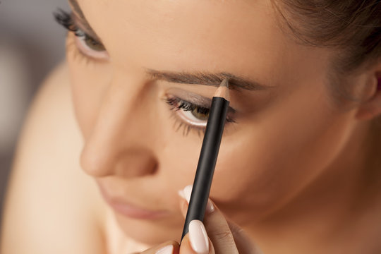 Young woman contouring her eyebrows with pencil on white background