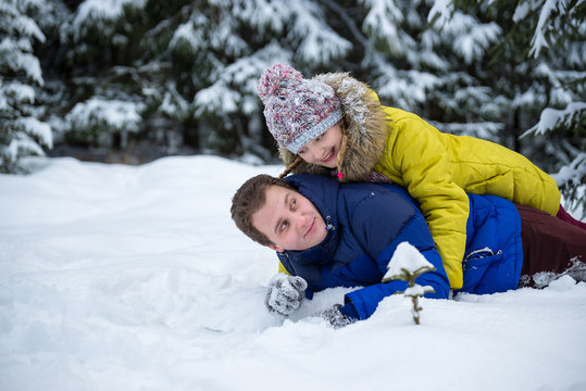 Happy young woman and man lay in snow on the ground in winter forest