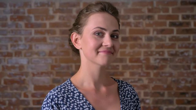 bautiful confident smile of young caucasian female, standing still and looking at camera with brick red wall behind